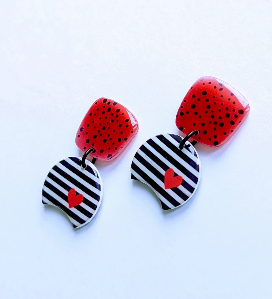 Two black and white striped earrings featuring small red heart charms hanging from them.