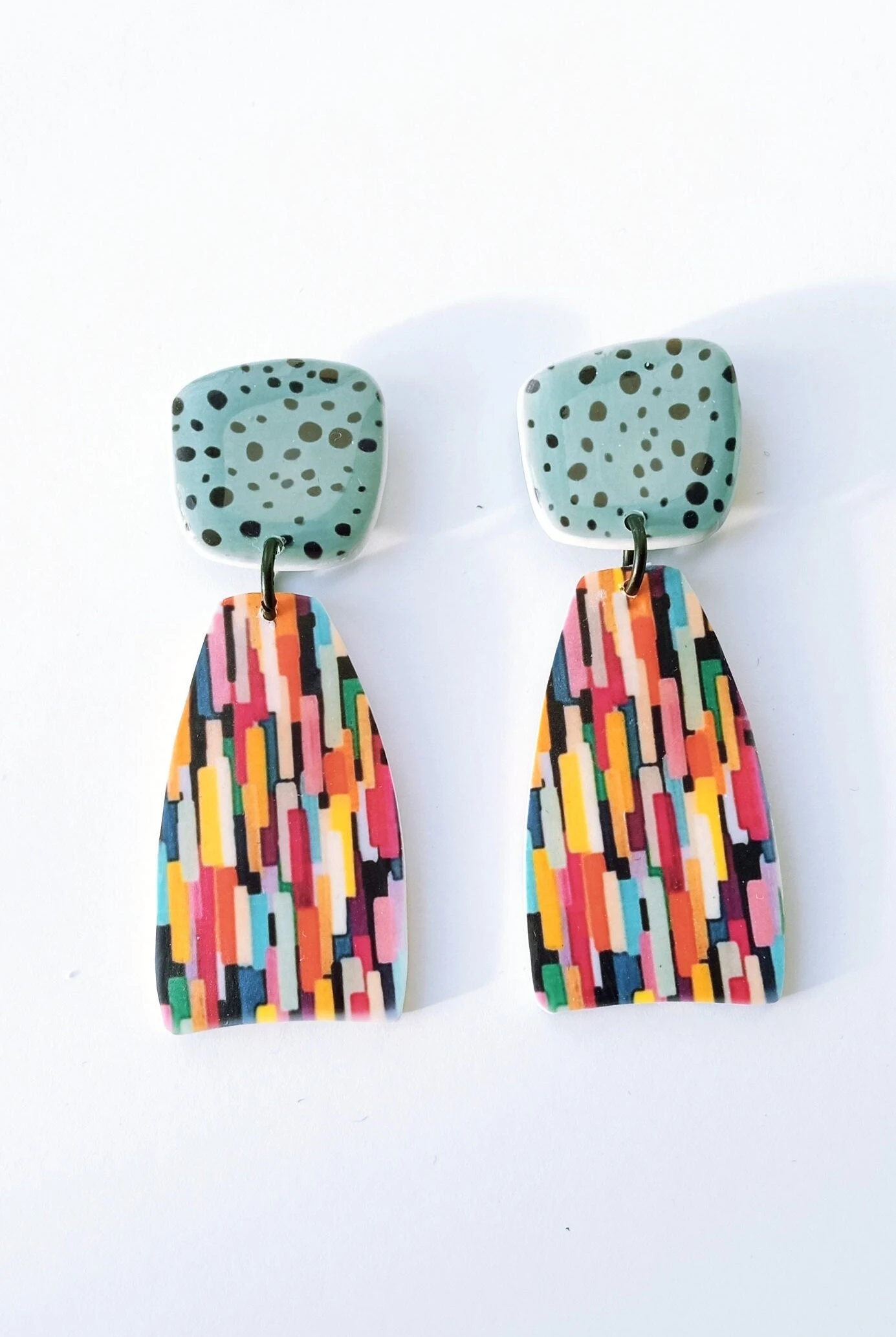 Abstract statement earrings with a blue top, black speckles, and a multicolored geometric pattern.