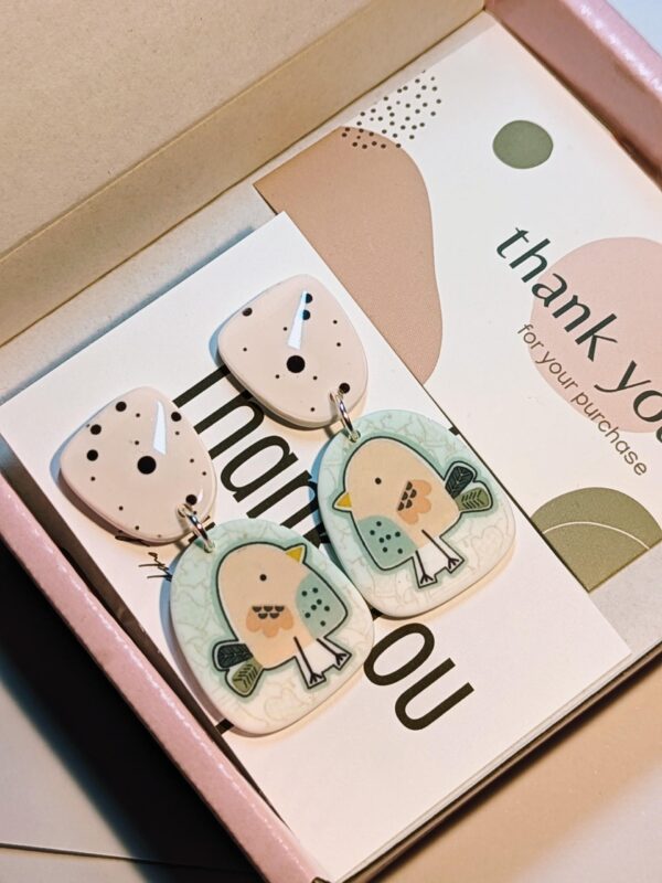 Artisan-made earrings with a bird and polka dot pattern in a box.