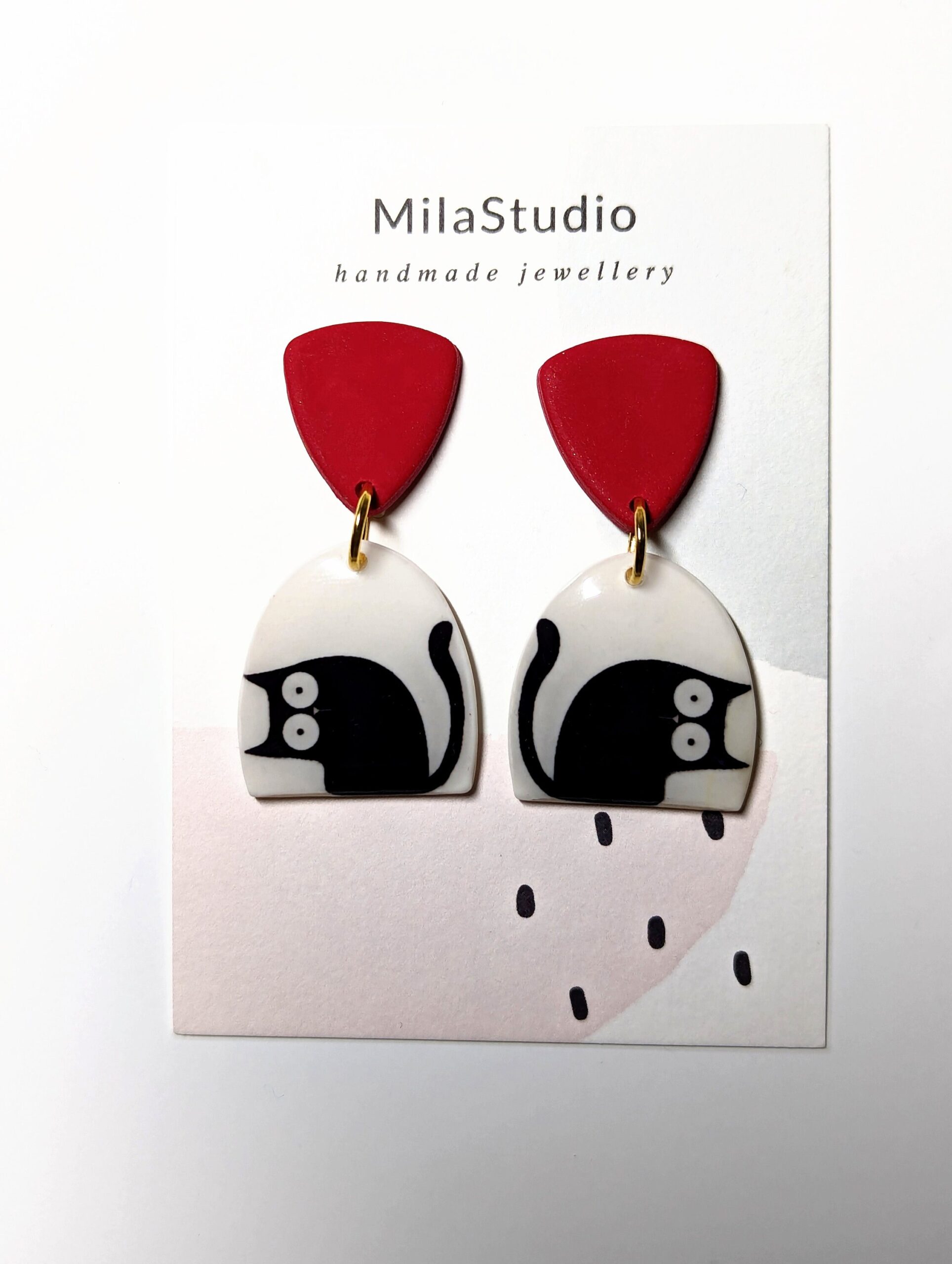 Handcrafted black cat earrings with a red top, on a white background.