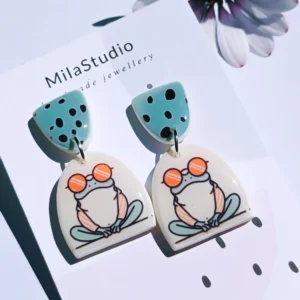 Playful frog earrings on a card with the Mila Studio logo