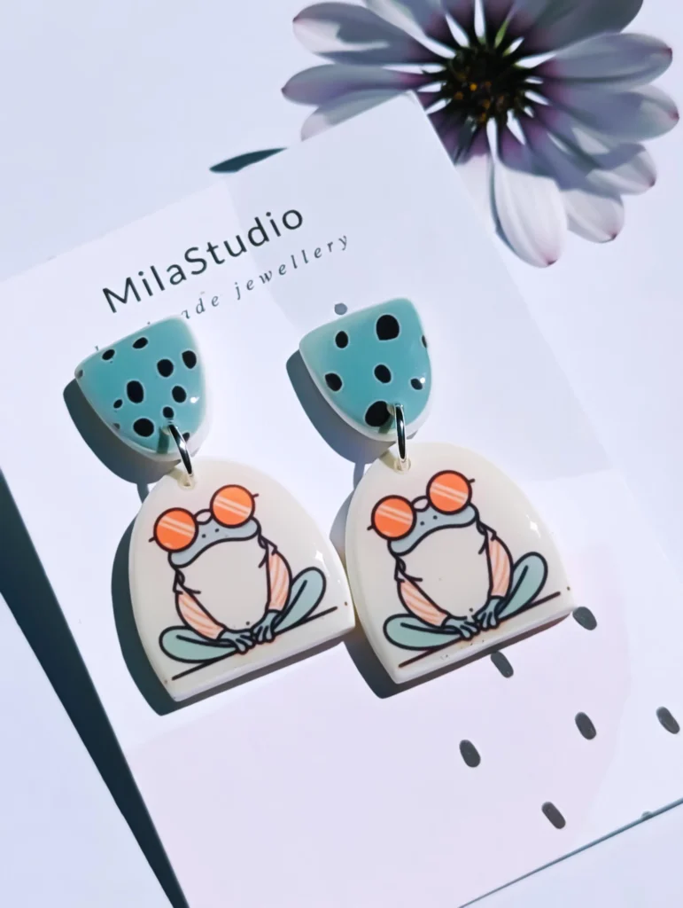 Playful frog earrings on a card with the Mila Studio logo