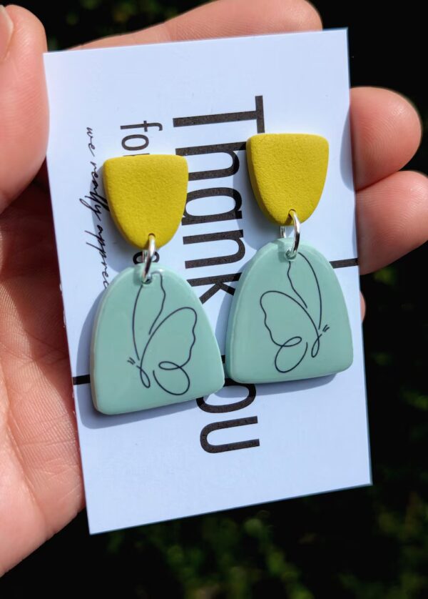 A hand holding butterfly earrings