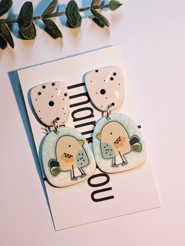 Bird earrings on a background with a plastic green plant