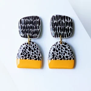 A pair of handmade yellow dangle earrings with a black and white abstract pattern.