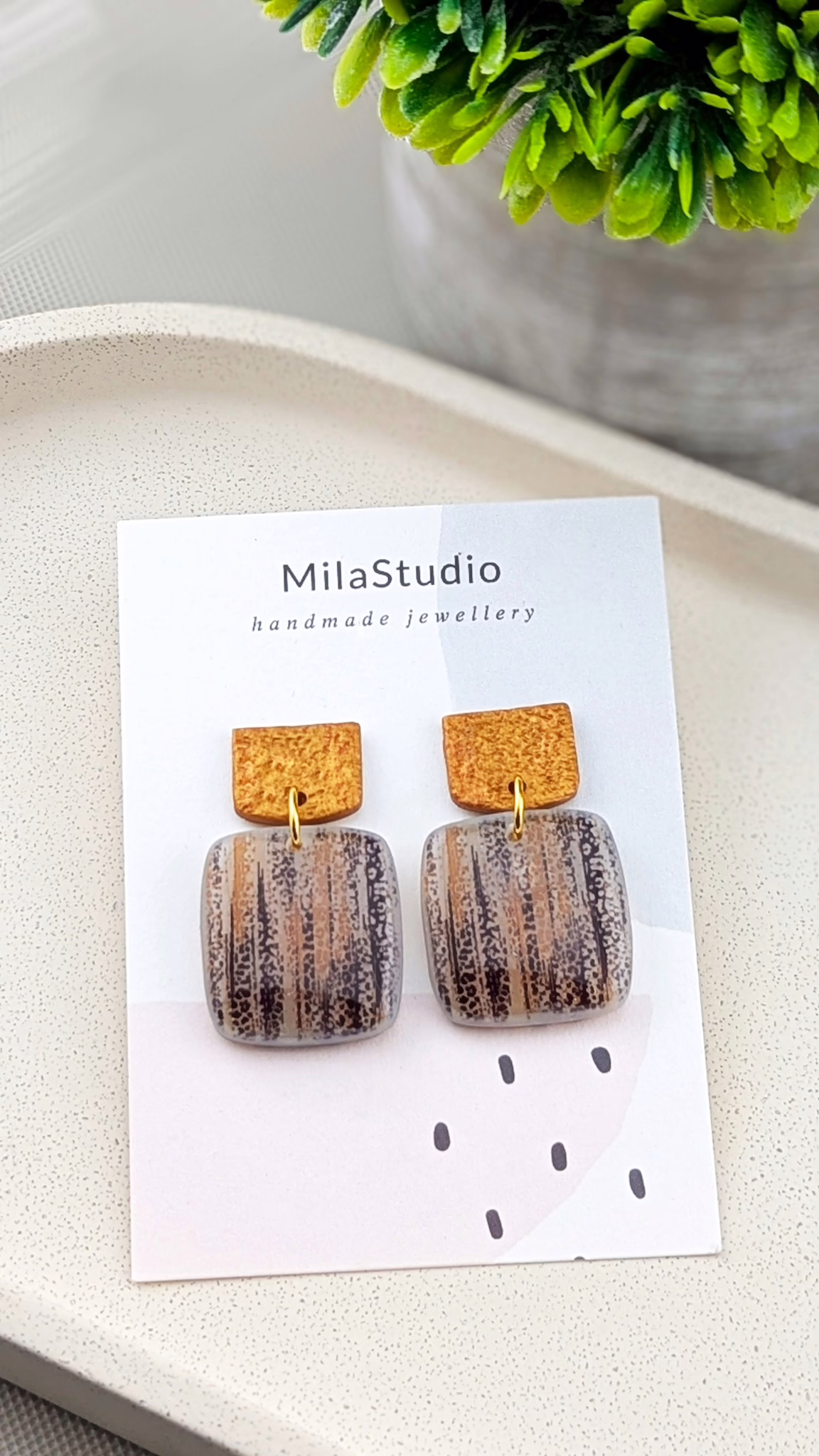 Close-up of textured earthy-toned earrings featuring black, cream, and gold colours.